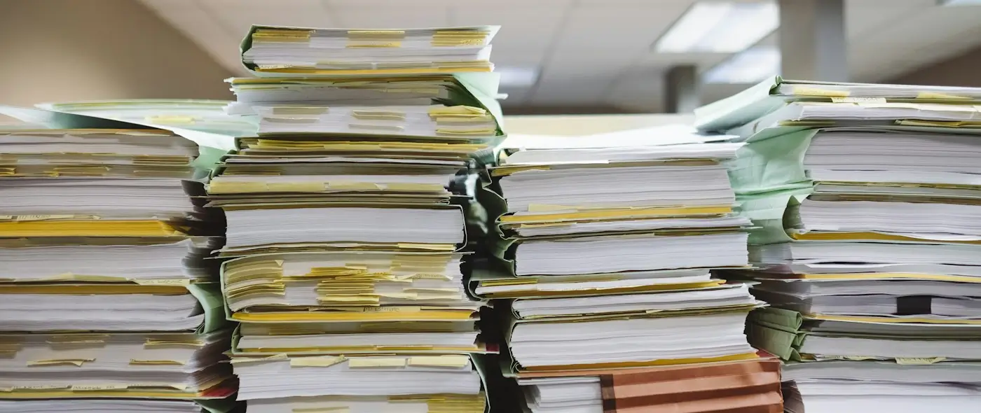 Stacks of paper documents and file folders on a desk