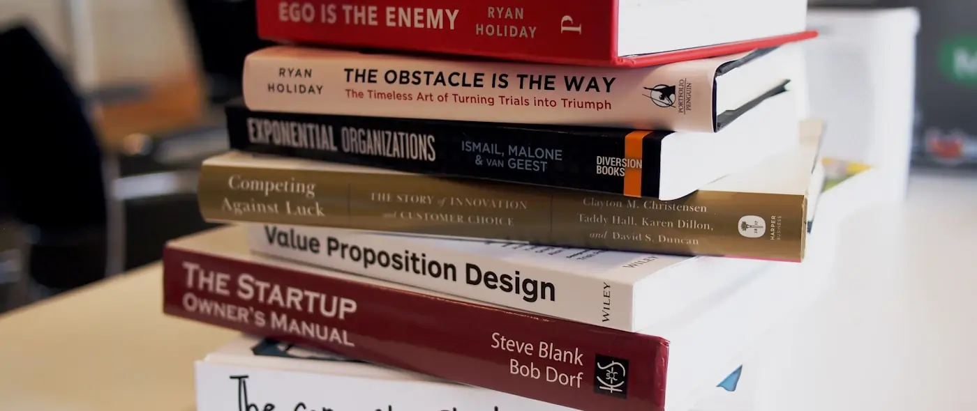 Stack of books on a wooden surface with reading glasses