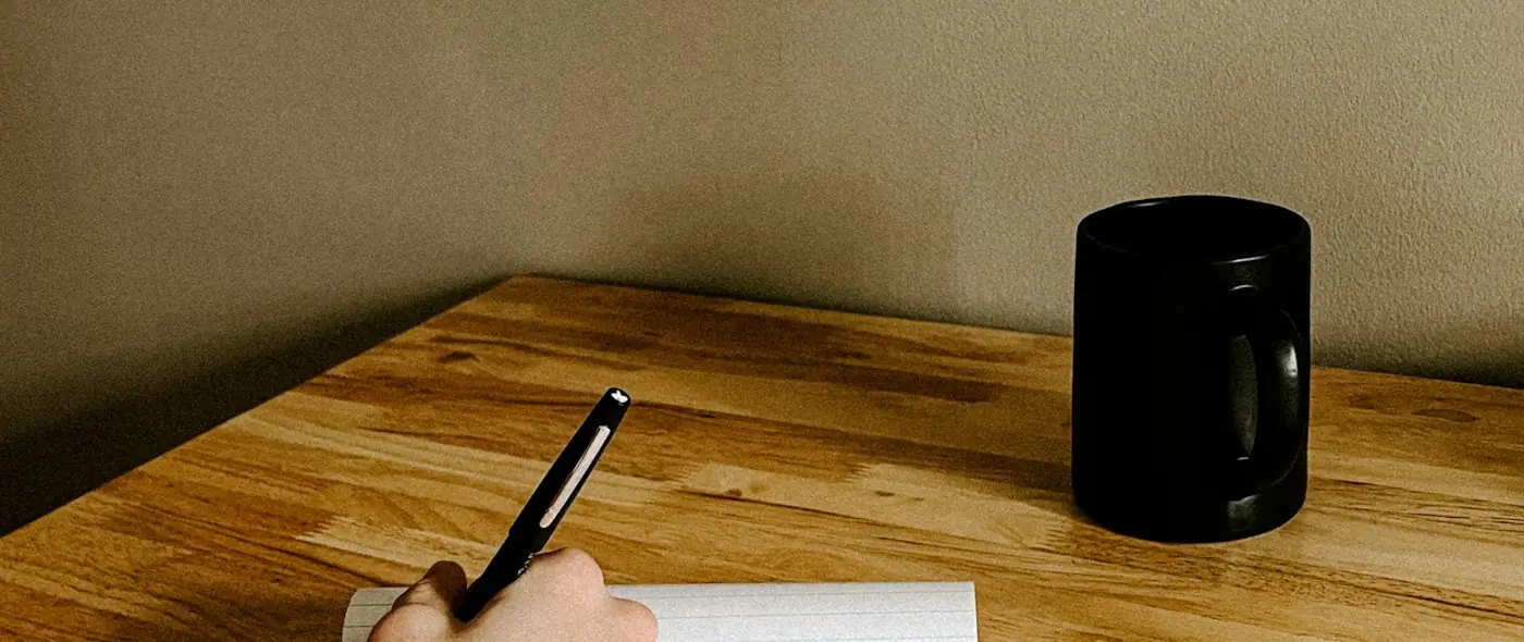 A hand writing notes on paper next to a keyboard, drafting a message