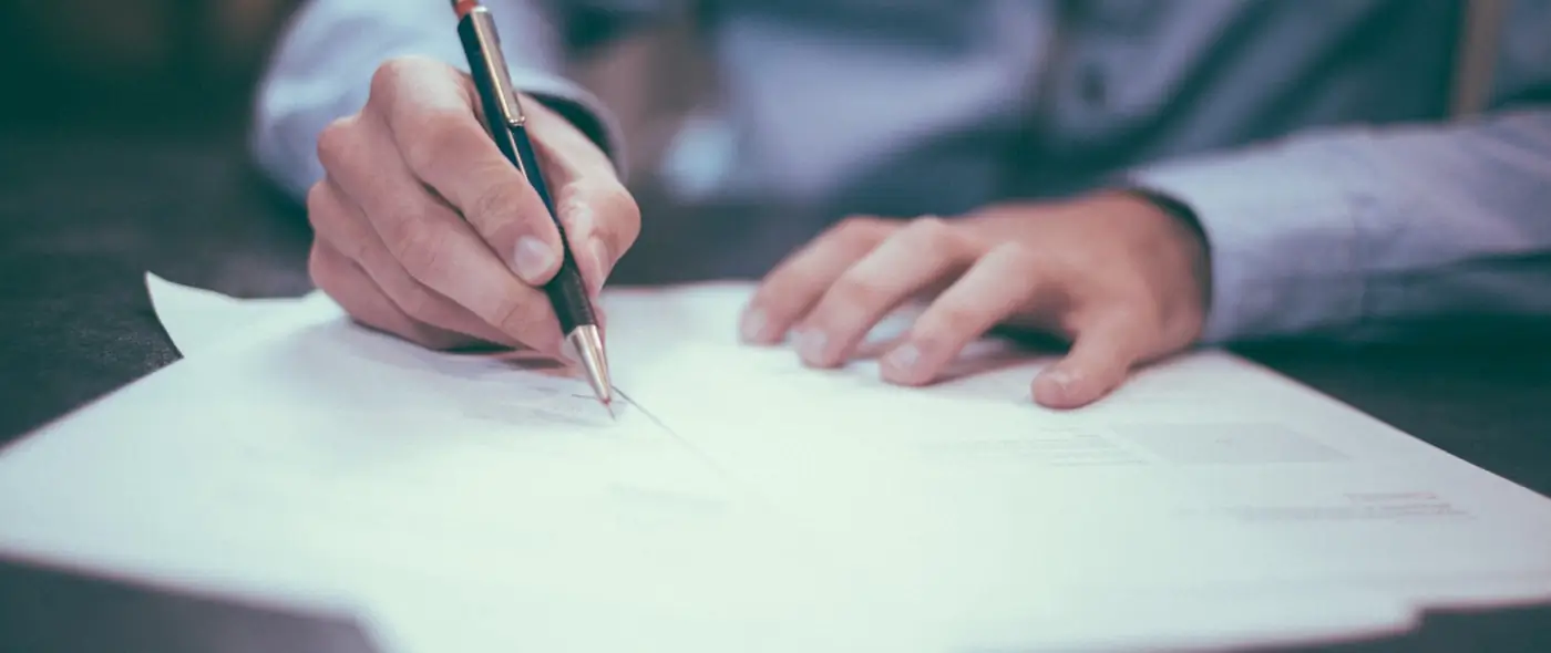 Professional signing a document at a desk with a pen