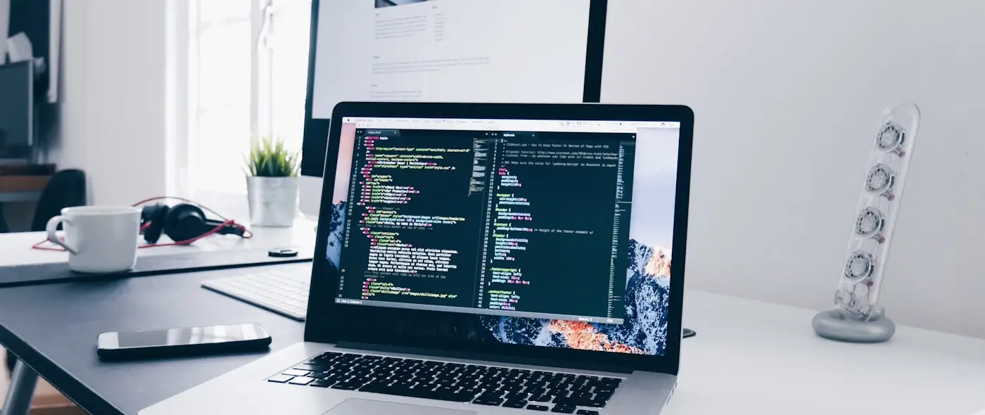 Laptop on a desk displaying code beside a mug and notebook